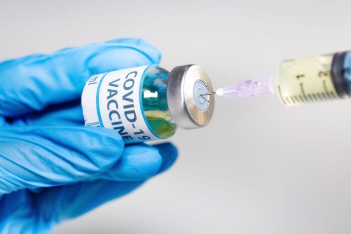 Coronavirus conceptual image of doctor hand in surgical glove holding a vaccine bottle with injection syringe in close up view